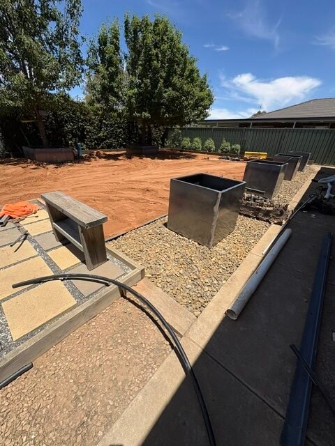 Bare backyard ground beside an outdoor entertaining area before turf installation.