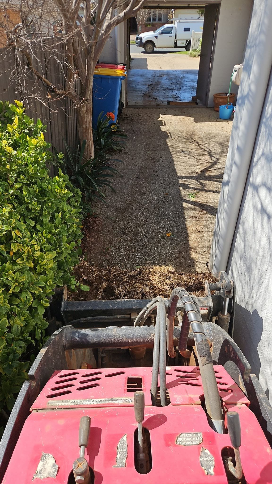 Compact landscaping equipment moving through narrow side access to a backyard.