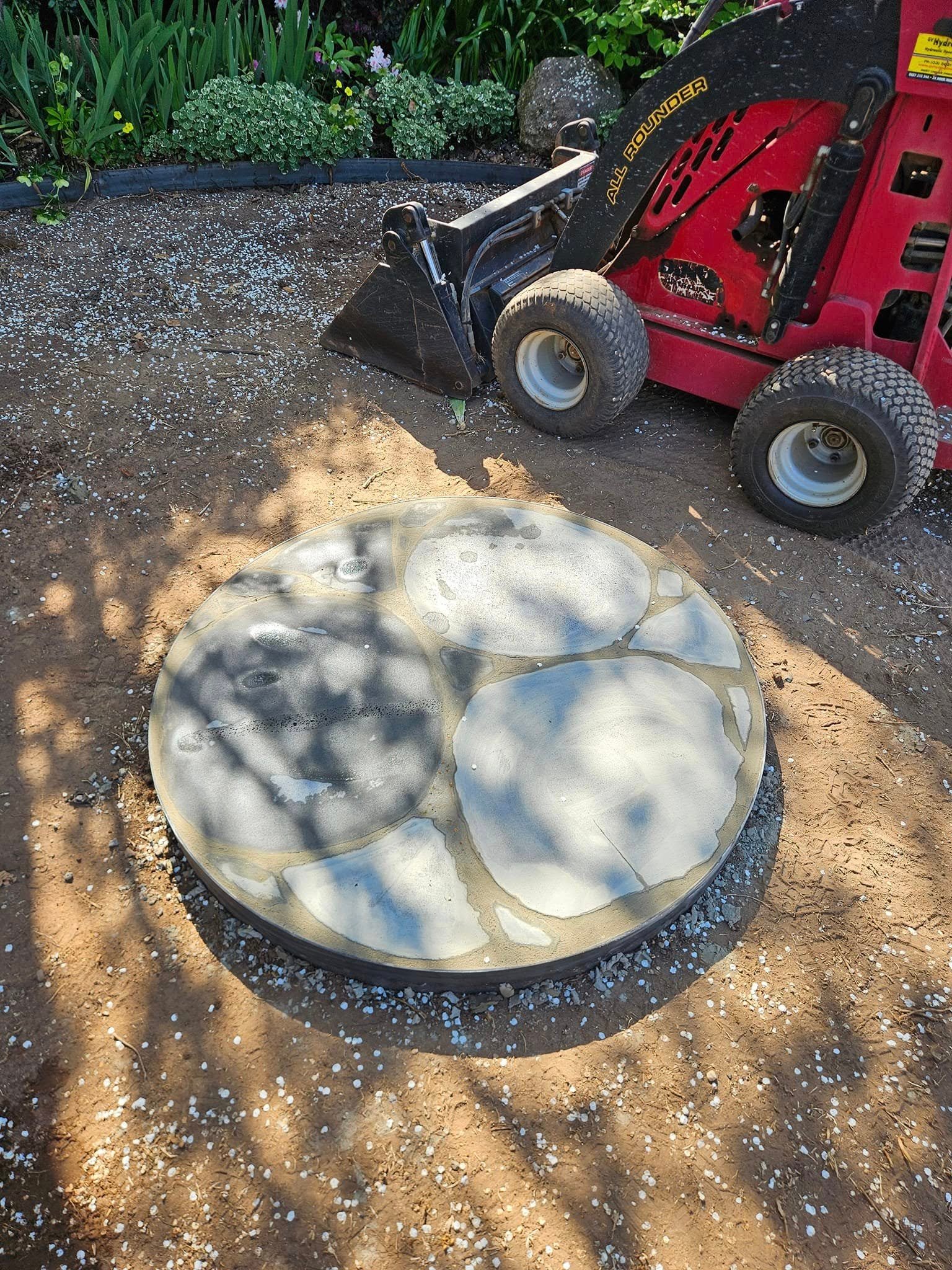 Circular custom fireplace platform under construction in a landscaped backyard.