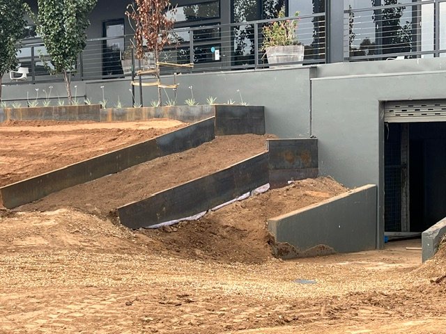 Corten steel retaining walls shape the sloping garden beside the building.