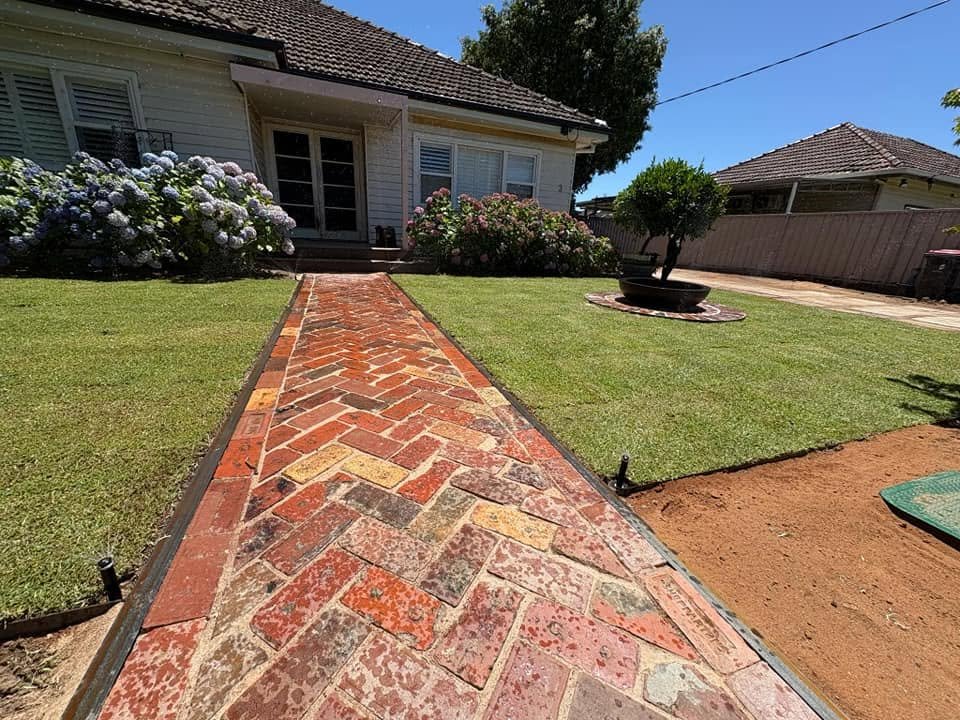 Completed herringbone brick path leading through new turf to the front entrance.